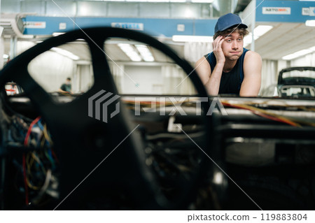 Portrait of confused mechanic male not knowing what disrepair during maintenance car in auto repair workshop. Doubtful repairman wearing workwear clothes, trying to solve problem. Portrait of confused mechanic male not knowing what disrepair during maintenance car in auto repair workshop. Doubtful repairman wearing workwear clothes, trying to solve problem. 119883804