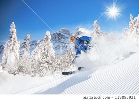 Skier skiing down a freshly groomed slope , beautiful panorama of high mountains during sunny day Skier skiing down a freshly groomed slope , beautiful panorama of high mountains during sunny day 119883921
