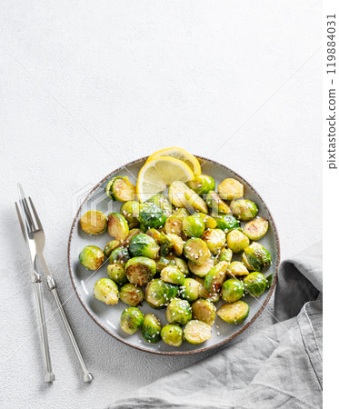 Fried brussels sprouts in a plate with soy or balsamic sauce, lemon and sesame on a light background Fried brussels sprouts in a plate with soy or balsamic sauce, lemon and sesame on a light background 119884031
