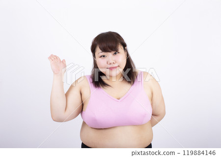 Fat young woman in a sports bra raising her right hand in front of a white background Fat young woman in a sports bra raising her right hand in front of a white background 119884146
