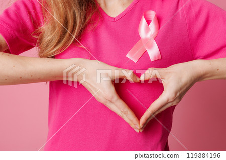 Young woman with pink ribbon making heart gesture on color background. Breast cancer awareness concept 119884196
