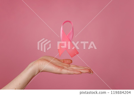 Female hands with pink ribbon on color background, closeup. Breast cancer awareness concept, pink ribbon symbolizing breast cancer awareness Female hands with pink ribbon on color background, closeup. Breast cancer awareness concept, pink ribbon symbolizing breast cancer awareness 119884204