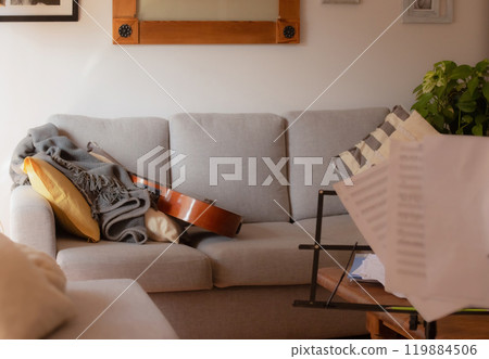 Music stand and sheet music in the foreground of a room. Guitar on the armchair Music stand and sheet music in the foreground of a room. Guitar on the armchair 119884506