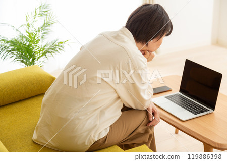 A middle-aged to senior woman sitting on a sofa in the living room at home looking at a computer 119886398