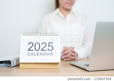 2025 Year Calendar on table with business woman using laptop computer, working and writing in office. countdown, Happy New Year, Resolution, Year End and New Start and Goals Plan Action Concept 119887306