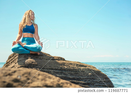 Yoga woman sitting in lotus position cliff rock beach sea blue sky Yoga woman sitting in lotus position cliff rock beach sea blue sky 119887771