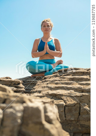 Yoga woman sitting in lotus position namaste hands cliff rock beach sea blue sky Yoga woman sitting in lotus position namaste hands cliff rock beach sea blue sky 119887785