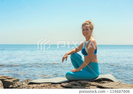 Yoga woman sitting in lotus position namaste hands cliff rock beach sea blue sky 119887806