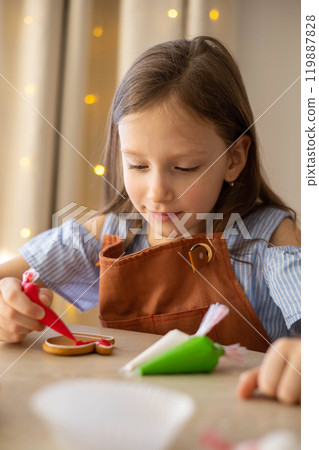 A little girl decorates a Christmas gingerbread mitten with icing. Concept Christmas A little girl decorates a Christmas gingerbread mitten with icing. Concept Christmas 119887828