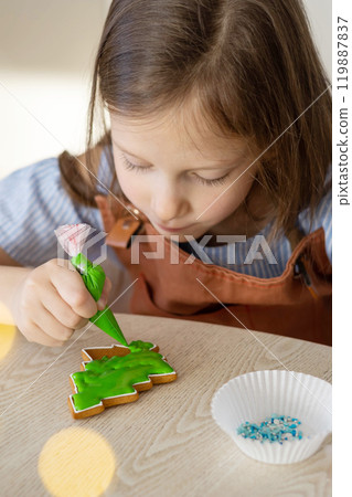 A little girl decorates a Christmas gingerbread mitten with tree. Concept Christmas 119887837