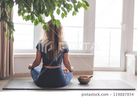 Smiling yoga woman meditation in lotus position listening music use headphones at home 119887854