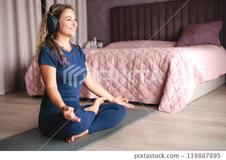 Smiling yoga woman meditation in lotus position listening music use headphones at home Smiling yoga woman meditation in lotus position listening music use headphones at home 119887895