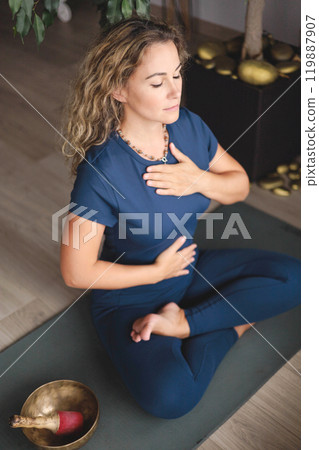 Yoga woman meditation in lotus pose with signing bowl sitting on mat at home 119887907