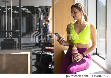 Fitness woman relaxing on mat use smartphone chatting at gym enjoy break Fitness woman relaxing on mat use smartphone chatting at gym enjoy break 119887927