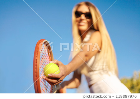 Woman tennis player tossing ball hitting racket at summer sunny outdoor court closeup Woman tennis player tossing ball hitting racket at summer sunny outdoor court closeup 119887976