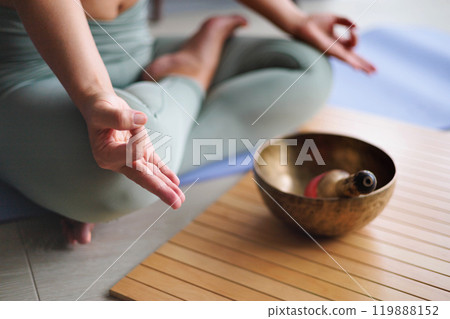 Woman in lotus position practicing yoga singing meditation bowl on wooden board top view closeup 119888152