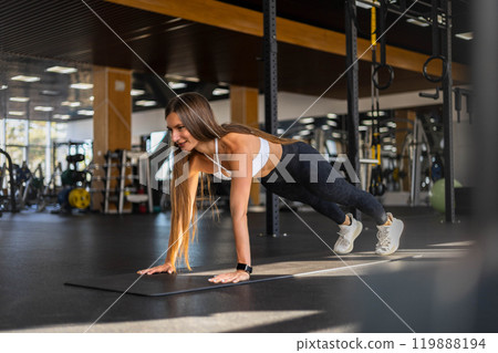 Smiling fitness woman stand in plank position doing push ups training at gym 119888194