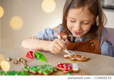 A little girl decorates a Christmas gingerbread mitten. Concept of preparations for Christmas 119888214
