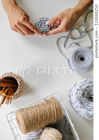 Women's hands crochet with gray yarn on a white background. Skeins of cotton yarn in natural 119888250