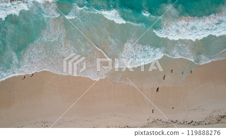 Aerial view of turquoise waves gently crashing onto a sandy beach. The oceans clear water, mixed with white foam, creates a tranquil 119888276