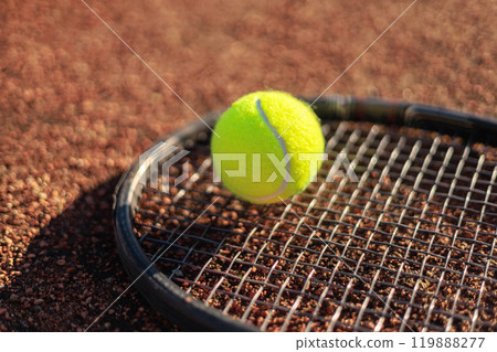 Yellow tennis ball lying on rocket at outdoor summer sunny court ground closeup 119888277