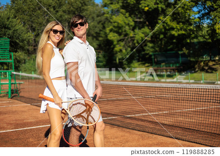 Smiling couple tennis players hugging posing together at outdoor summer sunny court 119888285