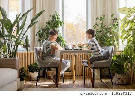 Boys brothers play chess at home at a round table on a chessboard. Children spend time actively  119888313