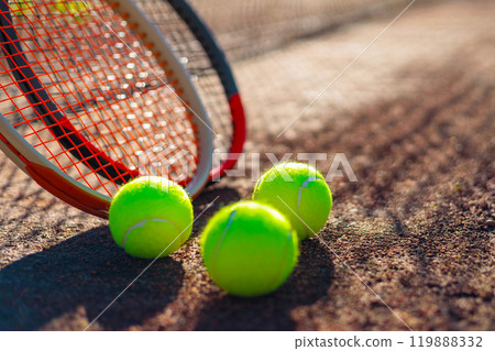 Tennis ball with rocket near grid at outdoor summer sunny court closeup Tennis ball with rocket near grid at outdoor summer sunny court closeup 119888332