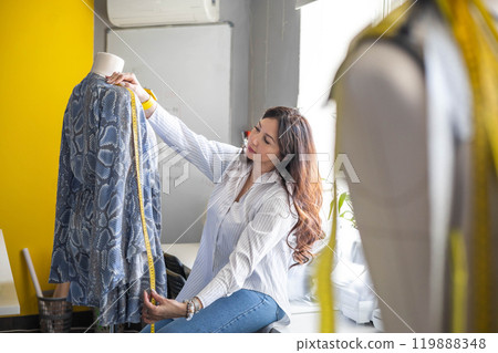 Plus size woman professional dressmaker tries on a dress on a sewing mannequin.  119888348