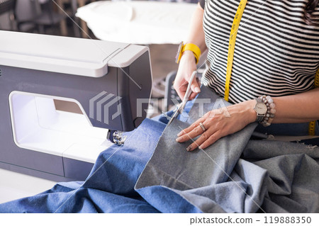 Beautiful young plus size woman dressmaker cuts out pattern pieces on denim and cuts clothes Beautiful young plus size woman dressmaker cuts out pattern pieces on denim and cuts clothes 119888350