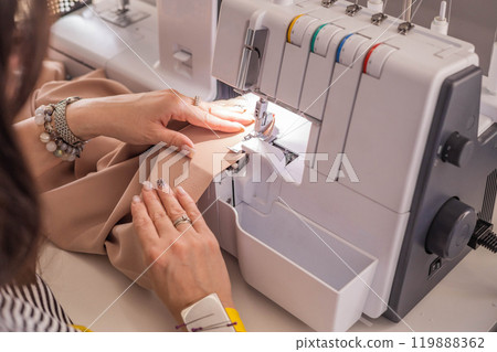 A plus size woman fashion designer uses an overlock sewing machine in her studio. A seamstress sews 119888362
