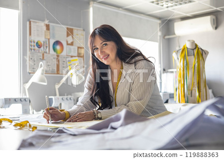 Beautiful young woman plus size dressmaker lays out pattern details on denim and cuts clothes Beautiful young woman plus size dressmaker lays out pattern details on denim and cuts clothes 119888363