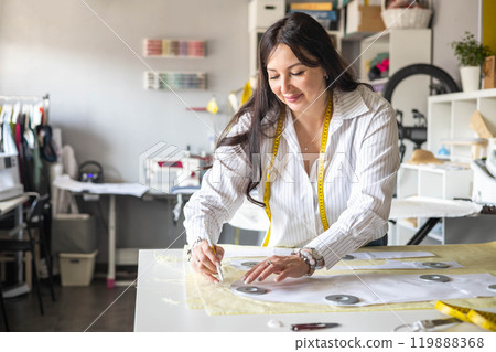 Beautiful young woman plus size dressmaker lays out pattern details on denim and cuts clothes Beautiful young woman plus size dressmaker lays out pattern details on denim and cuts clothes 119888368
