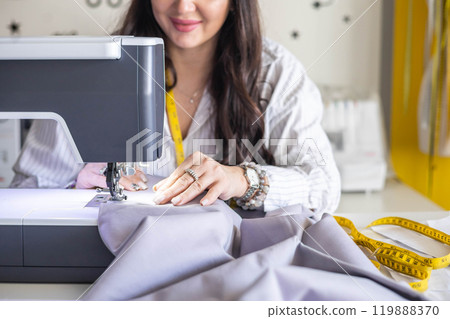 Woman plus size fashion designer uses a sewing machine in her studio. A seamstress sews clothes Woman plus size fashion designer uses a sewing machine in her studio. A seamstress sews clothes 119888370