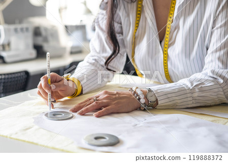 Beautiful young woman plus size dressmaker lays out pattern details on denim and cuts clothes Beautiful young woman plus size dressmaker lays out pattern details on denim and cuts clothes 119888372