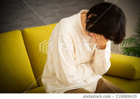 A middle-aged to senior woman feeling sad and covering her face on the sofa at home 119888420