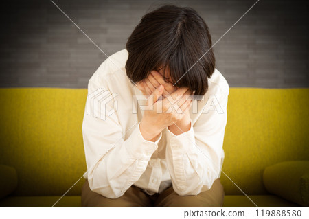 A middle-aged to senior woman feeling sad and covering her face on the sofa at home 119888580