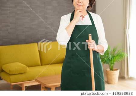 一位身穿綠色圍裙的高級女家庭主婦/管家在她家的客廳裡微笑 一位身穿綠色圍裙的高級女家庭主婦/管家在她家的客廳裡微笑 119888988