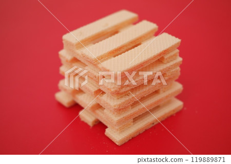 beige wafer cookies with a cream filling is scattered on a bright red surface 119889871