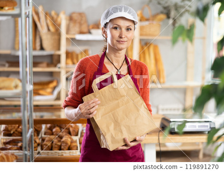 Woman entrepreneur owner of bakery holds out paper bag with pastries in hand Woman entrepreneur owner of bakery holds out paper bag with pastries in hand 119891270