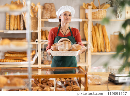 European female baker worker sells loaf of bread, shows many products 119891327