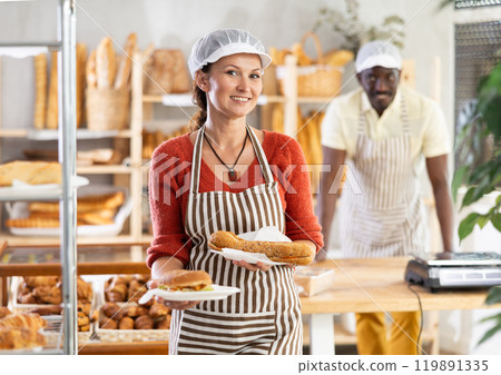 Positive woman baker holding plates with pastry 119891335