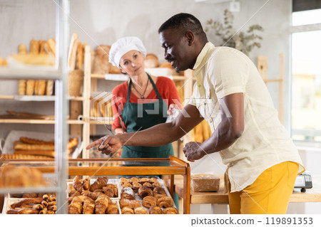 Man selects and buys hot croissants at a bakery. A female salesperson places croissants in bag Man selects and buys hot croissants at a bakery. A female salesperson places croissants in bag 119891353