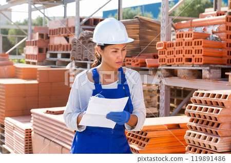 Woman with document in construction material storage 119891486