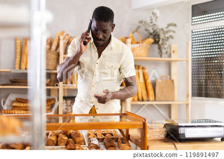Man standing at counter in bakery and talking on phone 119891497