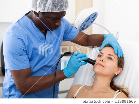 Young woman receiving face ultrasound lifting procedure in clinic Young woman receiving face ultrasound lifting procedure in clinic 119891669