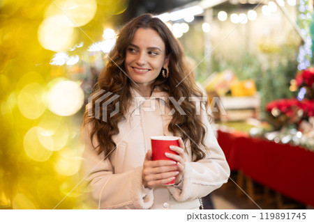 Happy woman walking through Christmas fair with cup of hot coffee Happy woman walking through Christmas fair with cup of hot coffee 119891745