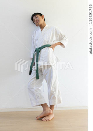 A boy in karate uniform leaning against a wall 119891756
