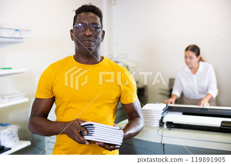 Happy middle-aged African American male typographer showing new notepads in the middle of the copy center 119891905