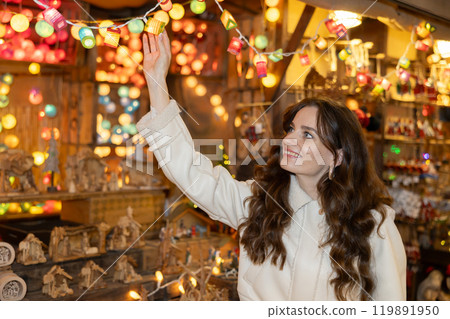 Young woman admiring colorful garland lights at street Christmas fair Young woman admiring colorful garland lights at street Christmas fair 119891950